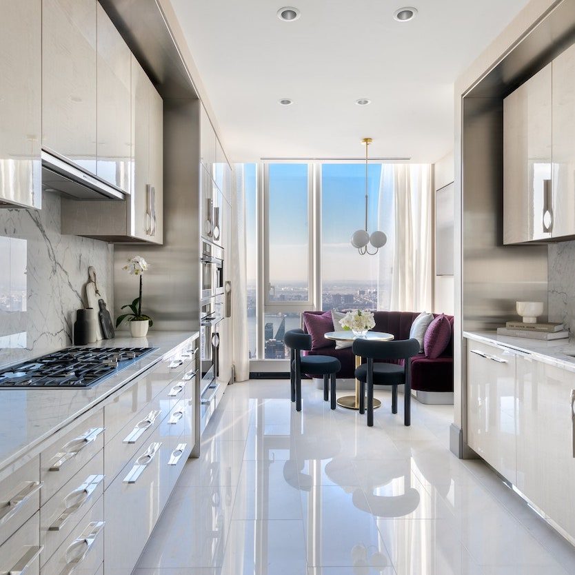 Modern kitchen with sleek cabinetry, marble countertops, and a dining area by large windows.
