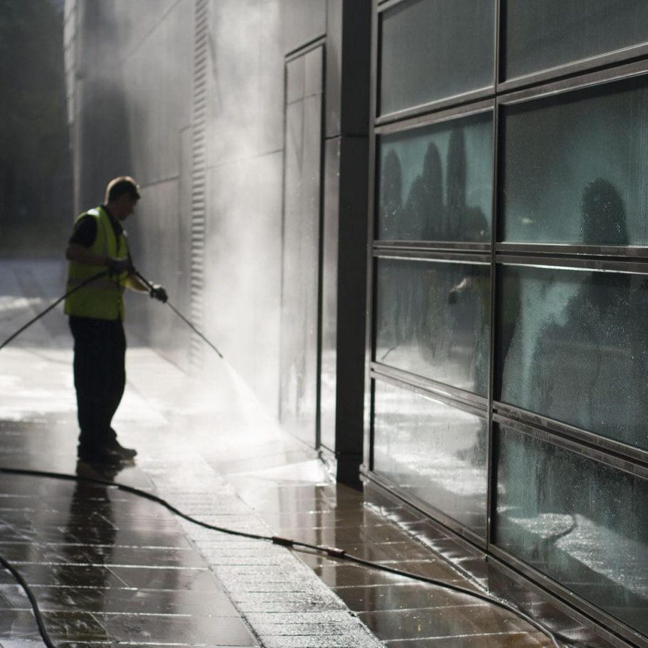 A person in a safety vest washes a building's exterior with a pressure washer.